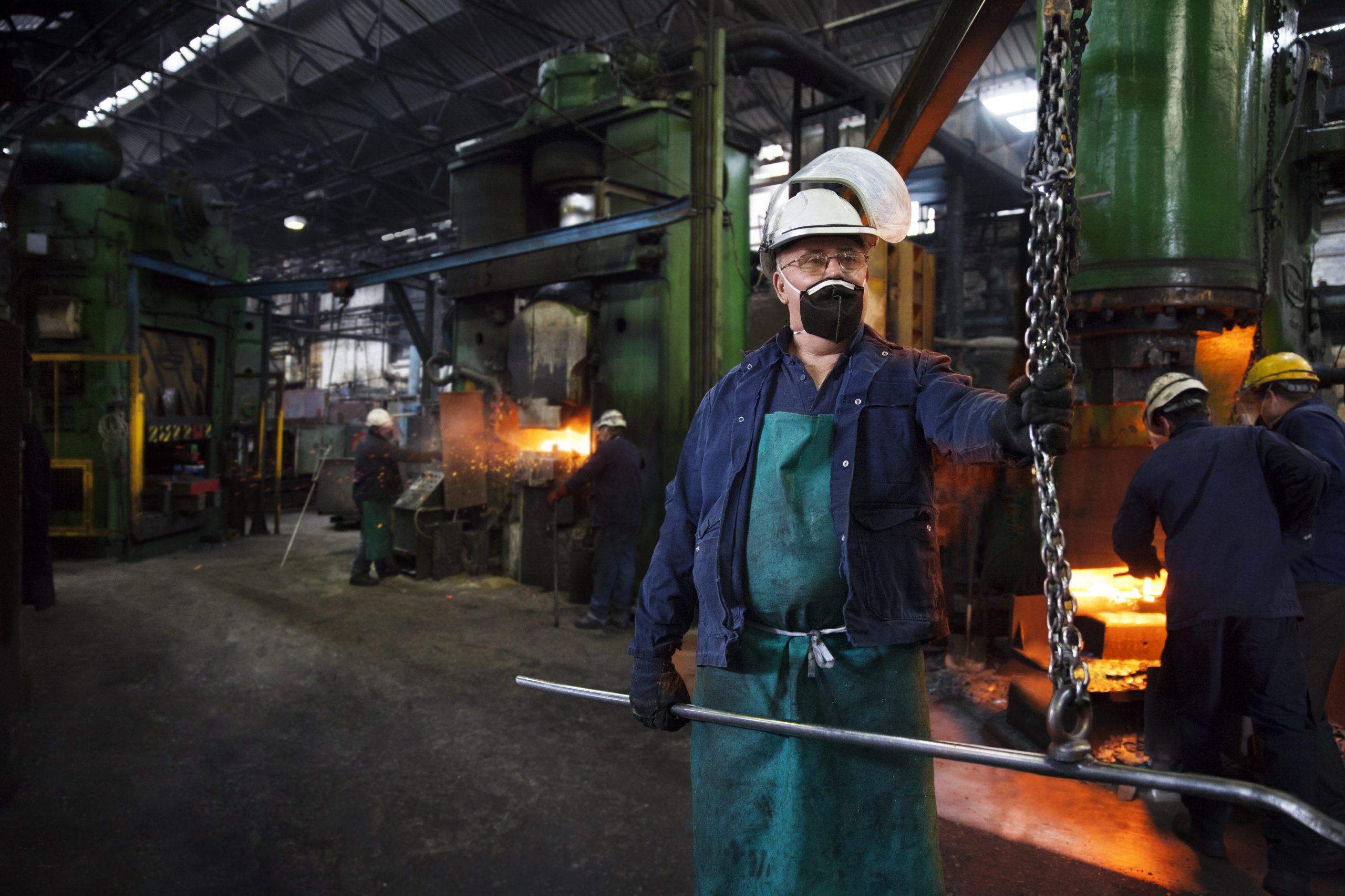 Operative prepares to hook steel billet out of furnace. Team in background using counterblow hammer